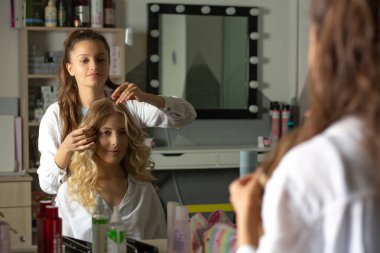 Kuaför, genç ve güzel bir kadın için sarı saçlar yaptıktan sonra kıvırcık yapar.