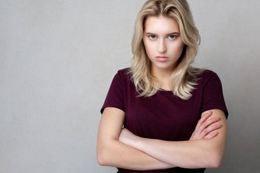 Gri bir stüdyo arka planında duran, kırmızı tişört giyen, gücenmiş genç bir kadın. Boş boşluk