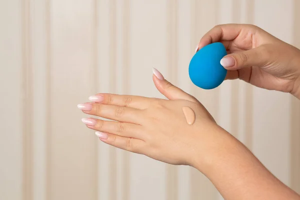 Woman applying liquid foundation with blue beauty blender from her hand. Space for text