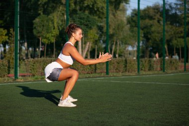 Formda bir kadın parkta çömelirken spor kıyafeti giyer. Metin için boşluk