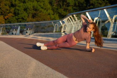 Muhteşem kızıl saçlı spor elbiseli kadın köprüde kalas egzersizi yapıyor. Metin için boşluk