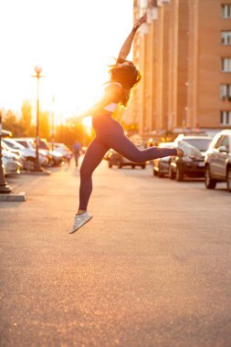 Atletik kaslı bir kadının altın bir akşam güneşiyle caddeye atlamasının yan görüntüsü