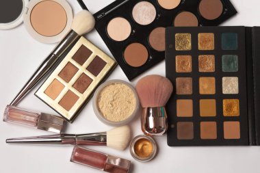 Düz göz gölgeleri, şekillendirme paleti, makyaj fırçaları, tozlar ve gri arkaplanda dudak parlatıcıları.