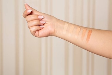 Woman applying shades from light to dark of a liquid makeup foundation on hand. Closeup shot clipart
