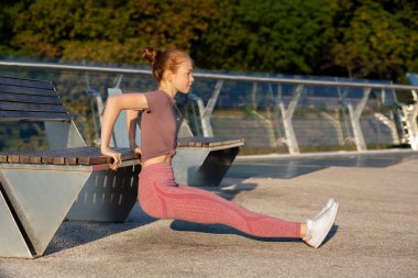 Atletik genç kızıl kadın sabahları bankta el egzersizi yapıyor. Metin için boşluk