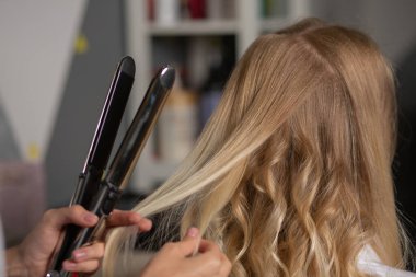 Bir kuaförün kuaför salonundaki müşterisine saç maşasıyla bukleler yaparken yakın plan fotoğrafı. 