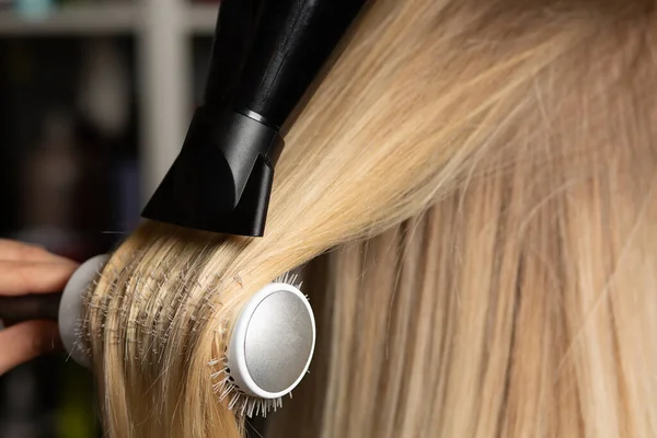 Professional hair stylist drying and straightens client\'s hair with a brush comb and a hair dryer