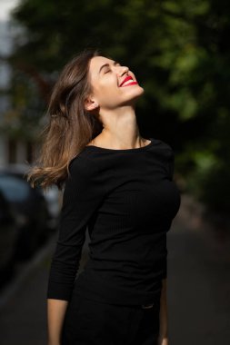Klasik siyah kıyafetler giymiş neşeli bir kadın yazın sokakta yürüyor.