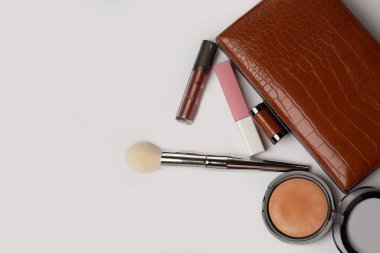 Bronz tozlu deri çanta, dudak parlatıcısı ve gri arka planda fırça. Boş boşluk