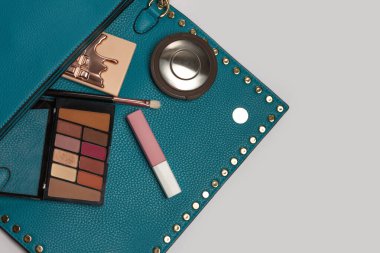 Moda konsepti: Basılı fosforlu kalem, göz farı paleti ve gri arkaplan üzerinde mat ruj olan kadın çantası. Boş boşluk