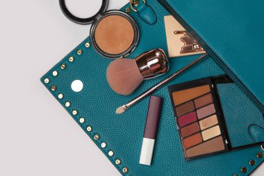 Moda konsepti: pres pudrası, kabuki fırçası, bronzlaşma tozu ve gri arkaplanda mat ruj bulunan kadın çantası. Metin için boşluk