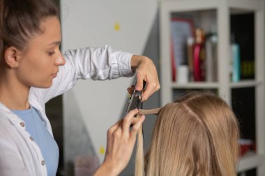 Kuaförde çalışma süreci: Kadın kuaför saç maşasıyla sarışın bir kadını kıvırtır. 