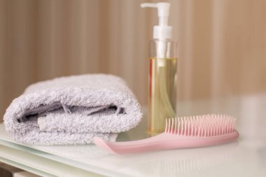 Bodrum yağını temizleyen bir şişe ve tarafsız bir bej arka planda bir masanın üzerinde banyo havlusuyla tarak. Metin için boşluk