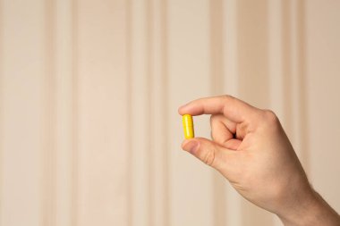 Bej çizgili arka planda C vitamini kapsülü tutan bir erkek. Metin için boşluk