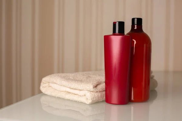 Bottles of hair shampoo and bath foam with towel on a desk over a neutral beige background. Space for text