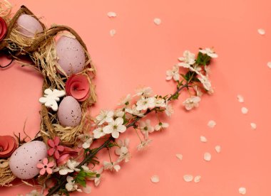 Renkli dekoratif yumurtalı Paskalya çelengi ve pembe arka planda taç yaprakları olan bir dal taze bahar çiçeği.