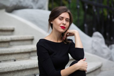 Kırmızı dudaklı ve kısa kıvırcık saçlı çekici bir kadının hayat tarzı merdivenlerde oturan modaya uygun siyah elbiseler giyiyor.