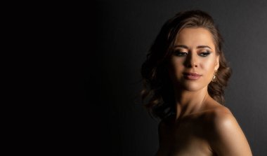 Profesyonel makyajlı, gölgeli çıplak omuzlarıyla poz veren muhteşem esmer bir kadının yakın çekim stüdyo portresi. Metin için boşluk