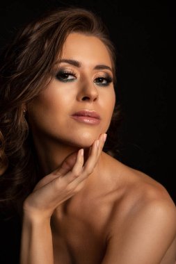Profesyonel makyajlı, gölgeli çıplak omuzlarıyla poz veren güzel esmer bir kadının yakın çekim stüdyo portresi.
