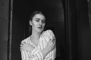 Beyaz çizgili gömlek giyen, üzgün, zarif bir genç kadının siyah beyaz portresi.