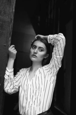 Tarz sahibi genç bir kadının siyah-beyaz portresi çizgili beyaz gömlek giyer.