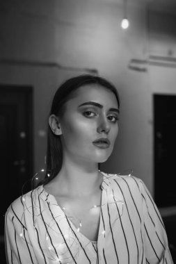 Siyah-beyaz, beyaz çizgili beyaz gömlek giyen hassas bir genç kadının portresi.