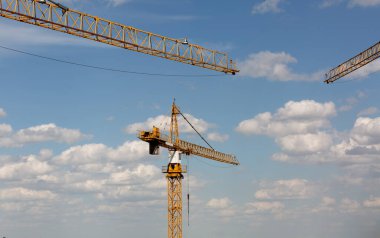 Çok katlı bina konsepti: gökyüzündeki inşaat alanında kule vinçleri ve arka planda bulutlar