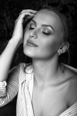 Doğal makyajlı şehvetli esmer kadın stüdyoda gözleri kapalı poz veren bir gömlek giyiyor. Siyah beyaz portre