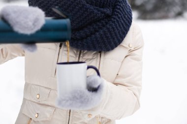 Genç bir kadın kışın sokakta termostan kahve döker.