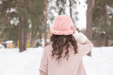 Güzel esmer, kıvırcık saçlı, örgü şapka takan ve kışın ormana bakan bir kadın.