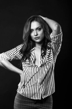 Uzun kıvırcık saçlı, çekici esmer kadın stüdyoda çizgili gömlek giyiyor. Siyah beyaz portre