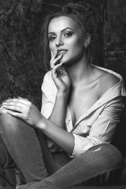 Hassas, esmer, doğal makyajlı bir kadın stüdyoda poz veren gömlek ve kot pantolon giyiyor. Siyah beyaz portre