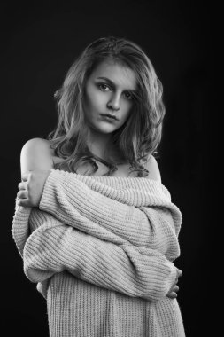 Uzun kıvırcık saçlı güzel esmer kadın gölgede poz veren çıplak omuzlu örülmüş bir kazak giyiyor. Tek renkli çekim.