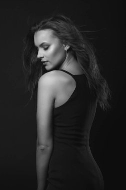 Mükemmel makyajlı ve saç stili olan esmer bir kadının moda stüdyosu portresi karanlık bir stüdyoda klasik siyah bir elbise giyer. Siyah ve beyaz çekim