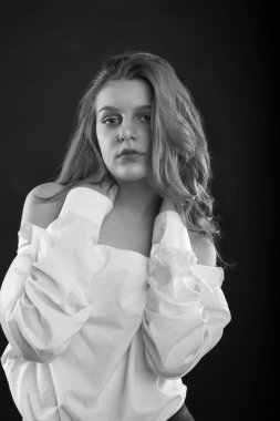 Şanlı genç kadın stüdyoda gölgede poz veren erkek gömleği giyiyor. Siyah ve beyaz resim