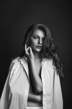 Seksi genç manken beyaz erkek gömleği giyer ve stüdyoda çıplak pozlar verir. Tek renkli çekim.