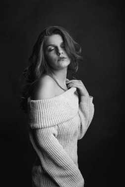 Uzun kıvırcık saçlı romantik esmer kadın gölgede poz veren çıplak omuzlu örülmüş bir kazak giyiyor. Tek renkli çekim.