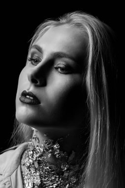 Parlak makyajlı ve boynundaki folyoyla gölgede poz veren şehvetli genç kadın. Tek renkli çekim.