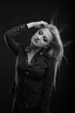 Mükemmel makyajlı ve rüzgarda saçı olan sarışın kadın stüdyoda poz veren bir bluz giyiyor. Siyah ve beyaz çekim