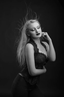 Parlak makyajlı ve uzun dalgalı saçlı baştan çıkarıcı genç manken dantelli korse giyer. Siyah beyaz stüdyo çekimi