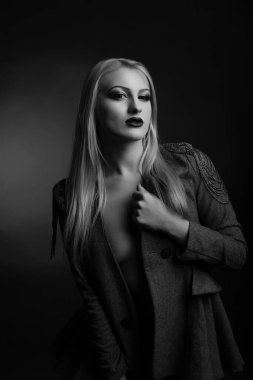 Parlak makyajlı ve uzun saçlı güzel sarışın kadın çıplak bir vücutta ceket giyiyor. Siyah beyaz stüdyo çekimi