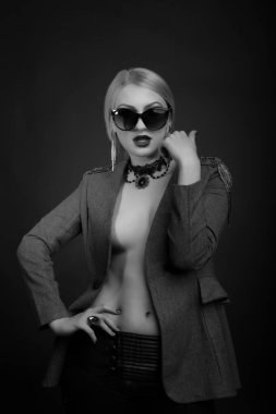 Baştan çıkarıcı sarışın bir kadının siyah beyaz stüdyo portresi çıplak bir vücutta güneş gözlüğü ve ceket takıyor.