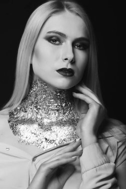 Siyah-beyaz güzellik çekimi: Stüdyoda boynundaki parlak makyaj ve folyoyla poz veren çekici sarışın model.