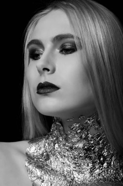 Siyah-beyaz güzellik çekimi: Stüdyoda parlak makyaj ve folyoyla poz veren zarif sarışın model.