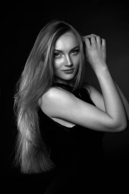 Uzun düz saçlı, şık bir genç kadın stüdyoda gölgede poz veren klasik siyah bir elbise giyiyor. Siyah ve beyaz çekim