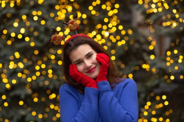 Güzel esmer kadın, Central City Meydanı 'ndaki Noel fuarında komik saç halkası ve kırmızı eldivenler takıyor.