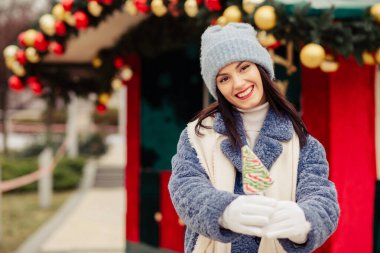 Mutlu esmer kadın örgü şapka ve kışlık palto giyiyor ve Noel arifesinde elinde toplarla şeker tutuyor. Metin için boşluk