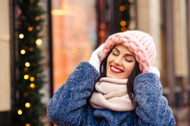 Neşeli esmer kadın, şehirde çelenklerle süslenmiş açık pembe bir şapka ve eşarp takıyor. Metin için boşluk