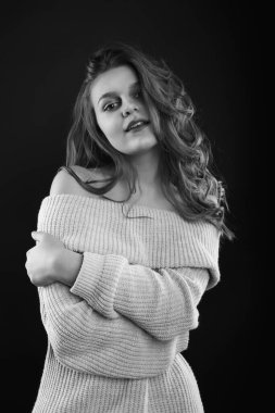 Uzun kıvırcık saçlı çekici esmer kadın gölgede poz veren çıplak omuzlu örülü bir süveter giyiyor. Tek renkli çekim.