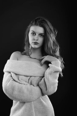 Uzun kıvırcık saçlı harika esmer kadın gölgede poz veren çıplak omuzlu örülmüş bir süveter giyiyor. Tek renkli çekim.